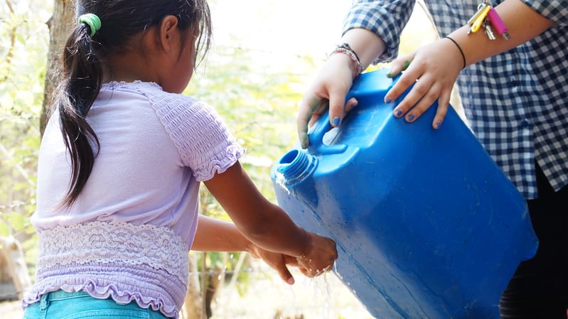 Young girl washing her hands with a bucket of water.