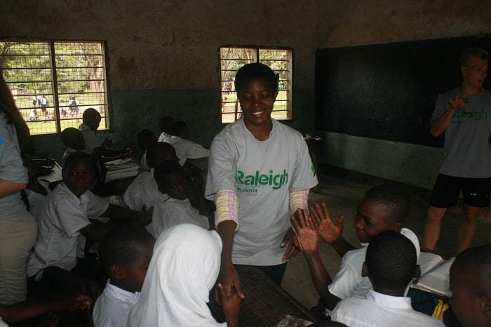 Tanzanian volunteer Mary shaking hands with schoolchildren in class to demonstrate how quickly germs spread