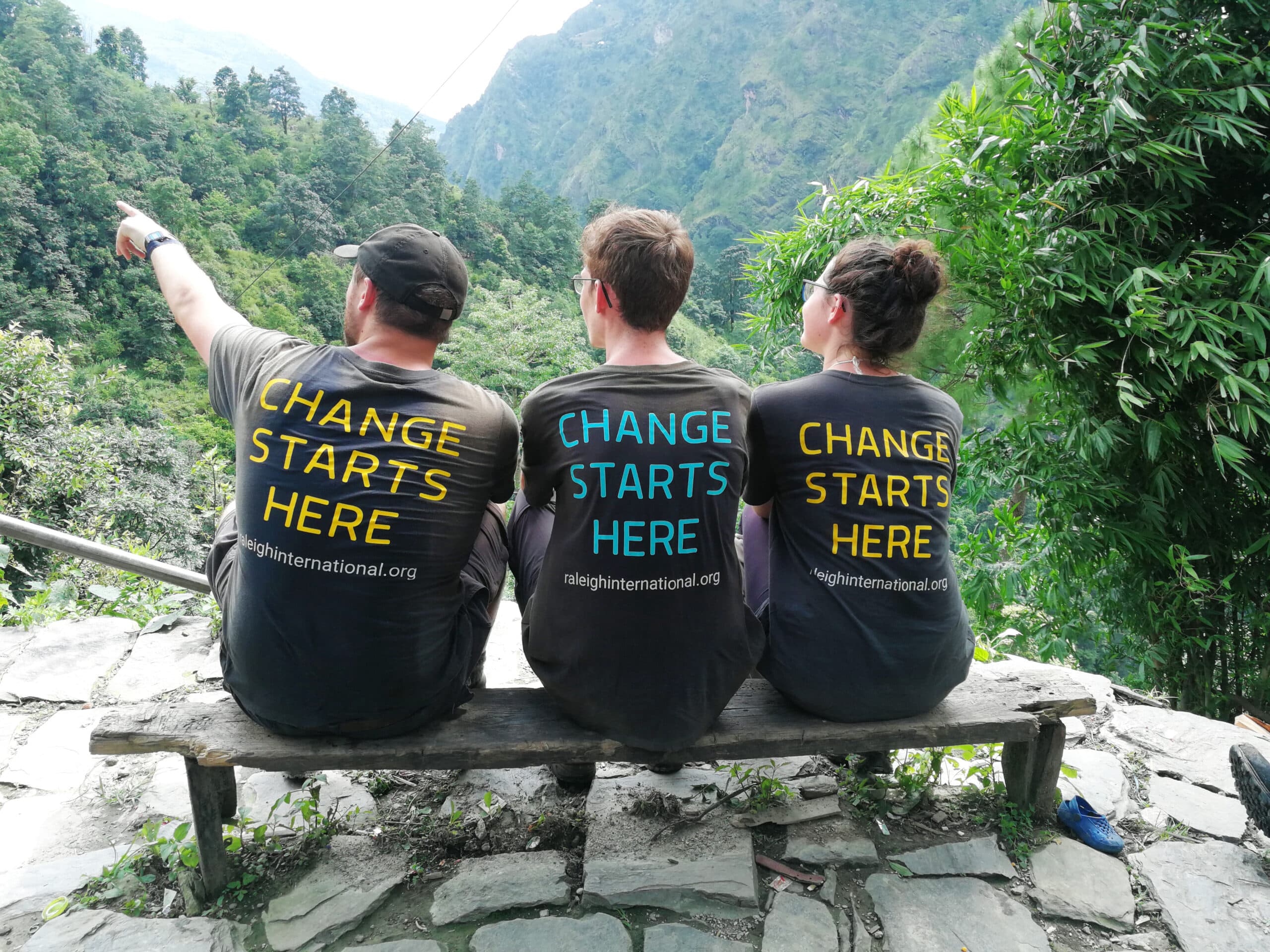 3 Raleigh International volunteers sitting with change starts here tshirts in a rainforest