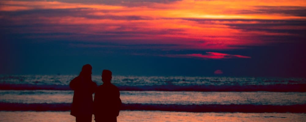 Couple looking at the the orange sunset at the beach