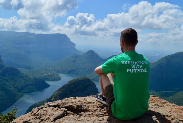 Volunteer sitting on mountain with amazing views while wearing a Raleigh International Tshirt