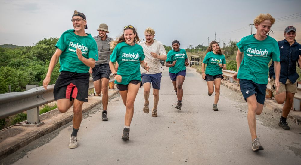 a group of Raleigh volunteers running together on a bridge