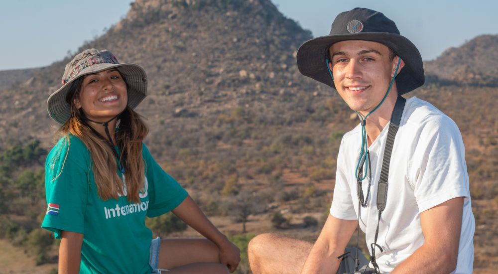 Two Raleigh volunteers, each wearing a hat, smiling at the camera.